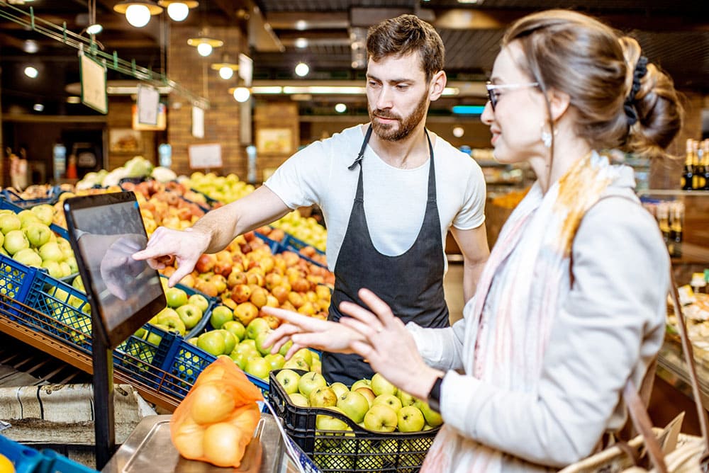 ragazza che pesa sulla bilancia frutta al supermercato e commesso che la aiuta